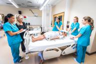 instructor and students standing around a hospital bed with mannequin patient