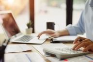 close up of hands working on balancing budget at table with notebook, bills, and calculator