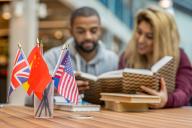 Two students sitting at a table reading language books with a jar with small international flags on the table in front of them