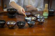 close up of hand holding ladle pouring tea into cups arranged in a half circle 