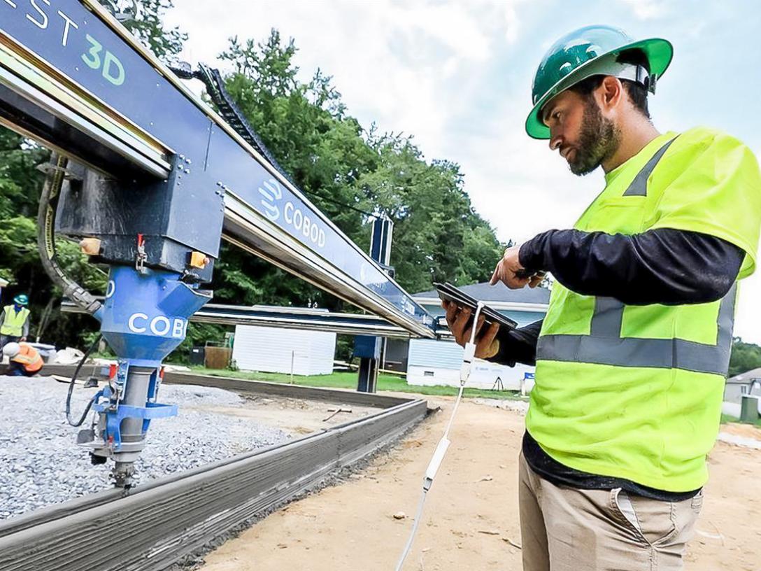 Alquist 3D team member collaborates with a 3D printing robot on a worksite