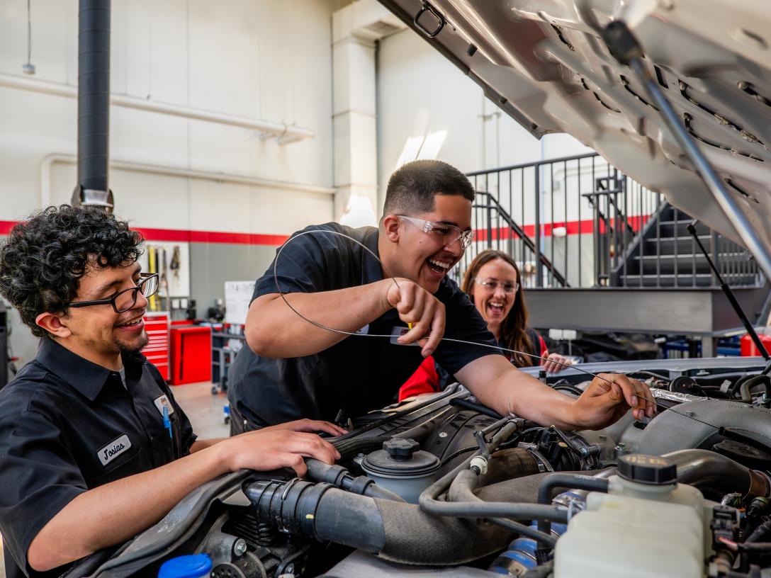 3 students learning how to check the oil levels in a pickup truck, laughing