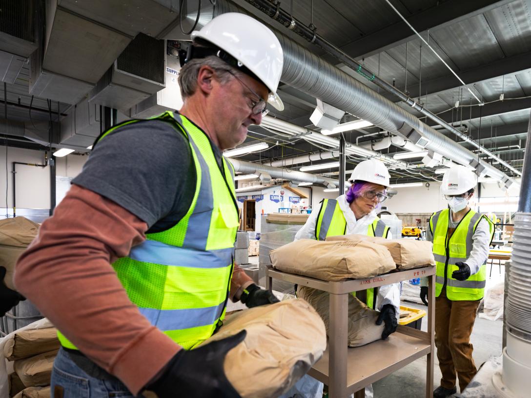 People in safety gear pour bags of additives into 3D printing robot