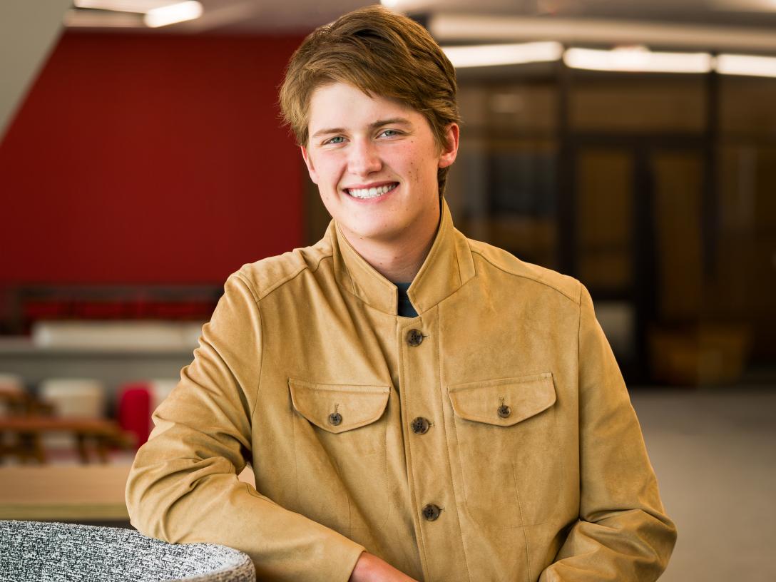 Gabriel stands leaning against a table in an Aims building smiling.