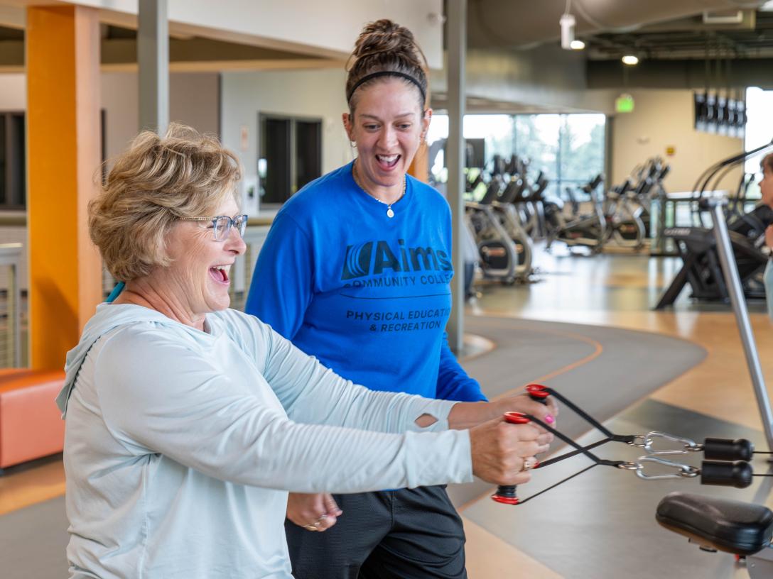 A  woman assisting another woman at the gym, demonstrating care and support during their workout session.
