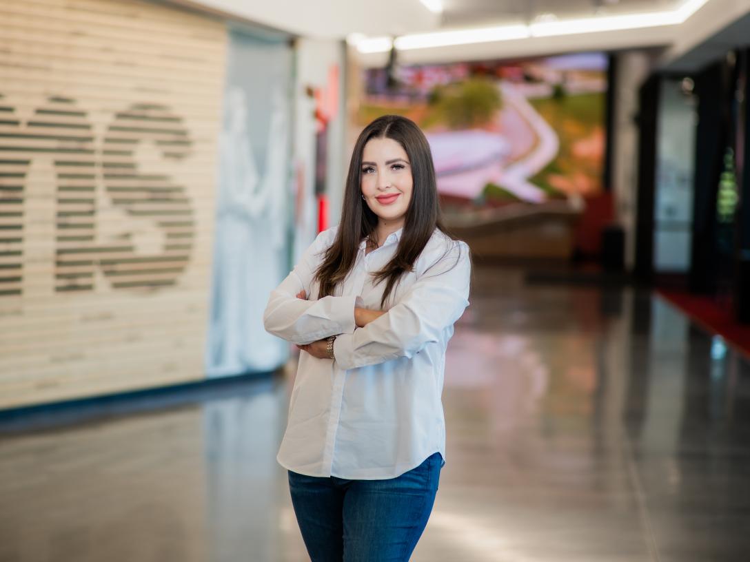 Priscilla Ortega Lozano stands in front of Aims logo on wall with arms crossed 