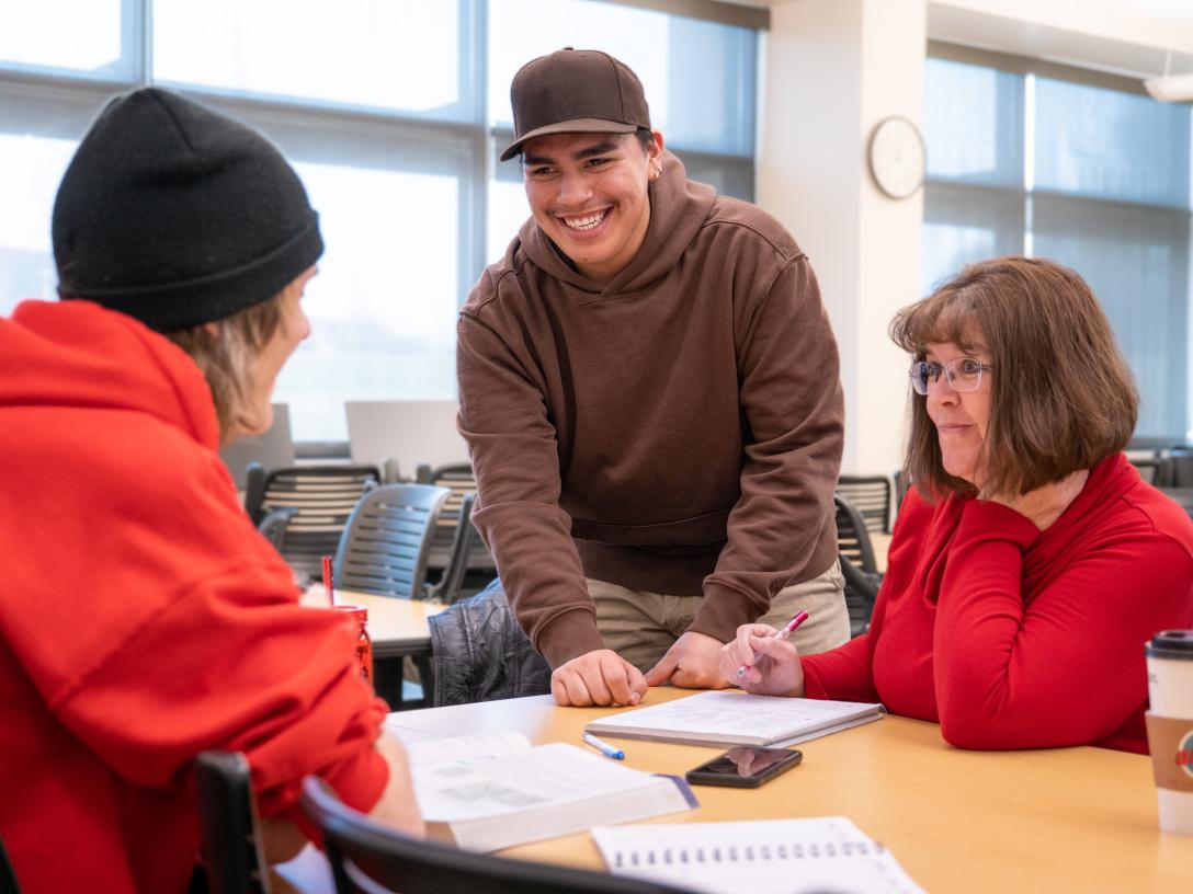 Students and teacher talk and smile at a table