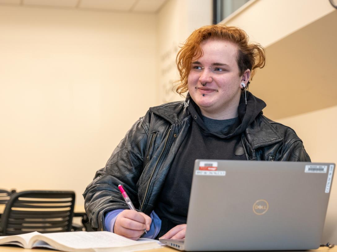 A student working at a desk with a pencil and a laptop