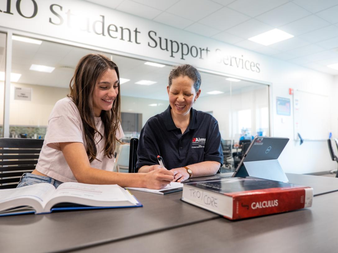 Tutor helping student study at a desk with books