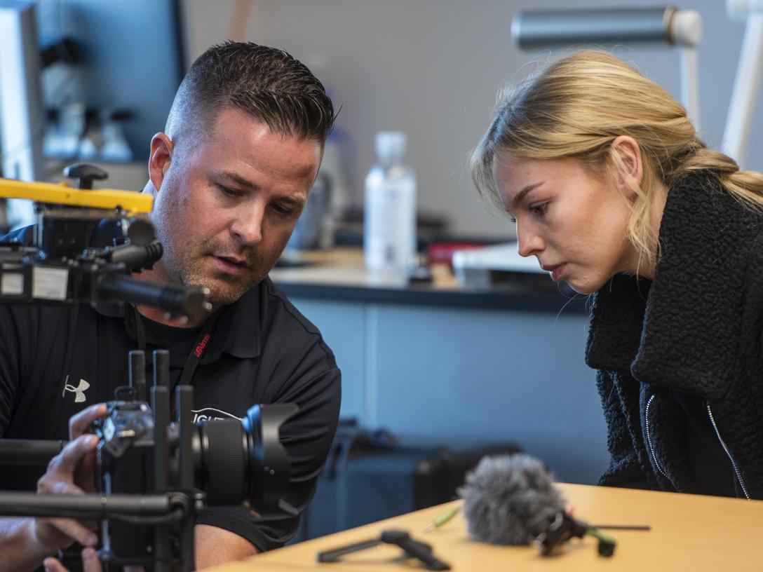 Two people sit at a table examining a camera on a UAS