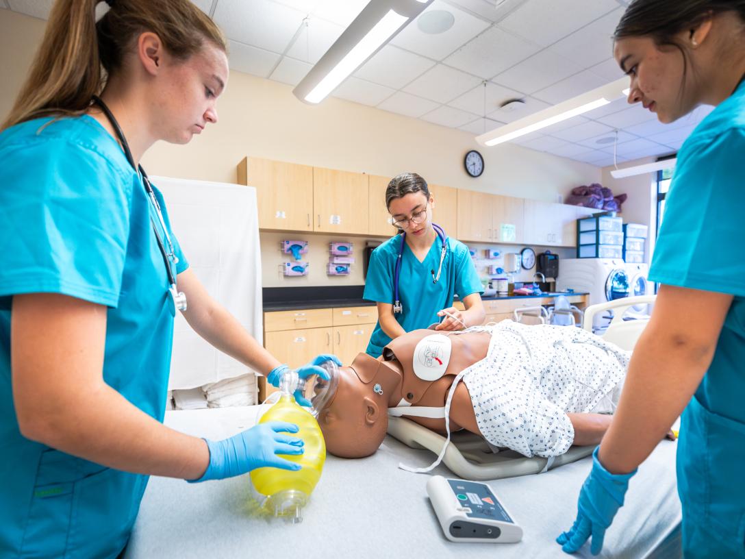 three students attending to a mannequin in a hosptal bed
