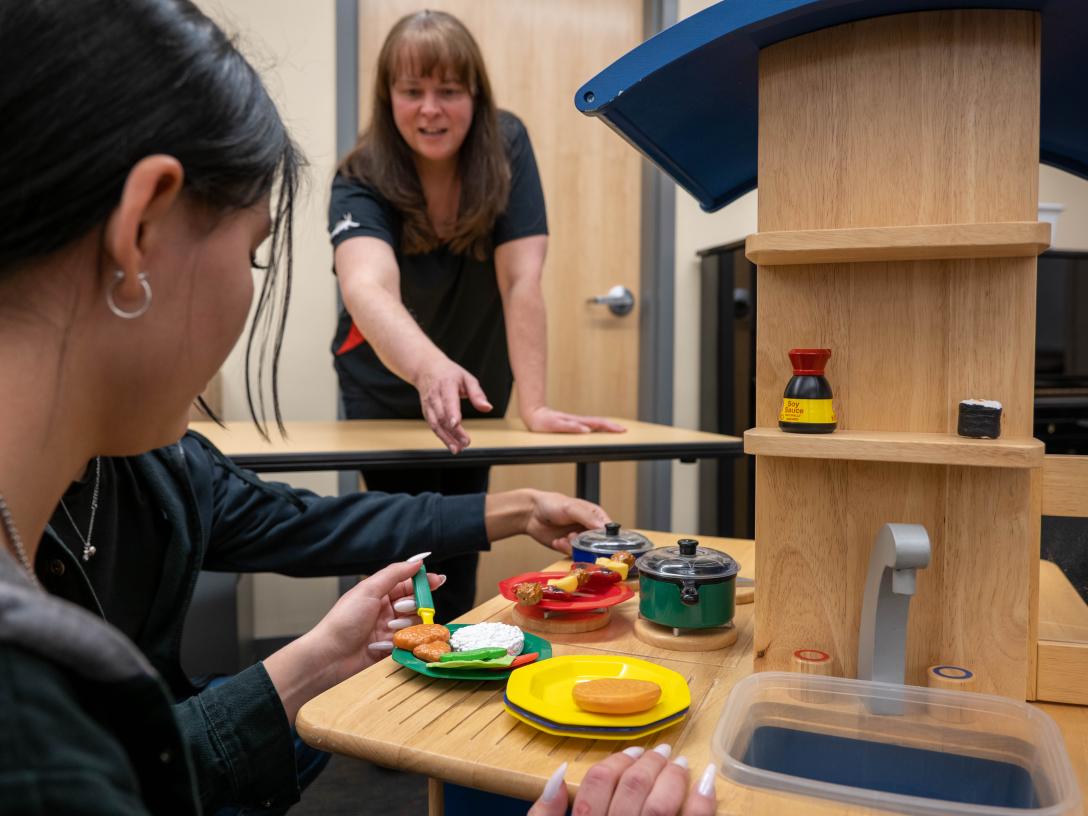 Aims early childhood education degree program students and instructor working with a play kitchen and food