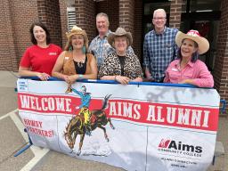 Group standing in front of sign saying, "Welcome Aims Alumni."
