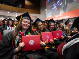 row of aims graduations holding their diplomas 