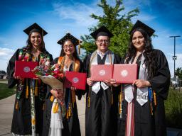 4 students with diplomas after graduation in caps and gowns