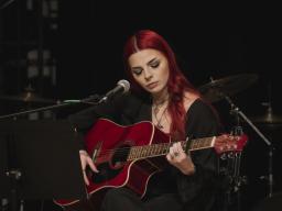 female on stages playing guilar in front of a microphone