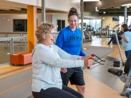 An Aims personal trainer helping a person to use exercise equipment at the PERC