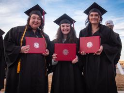 3 females in caps and gowns with diplomas