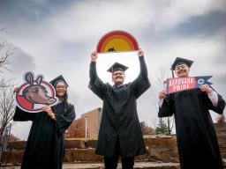 3 students in cap and gown with Aims signs