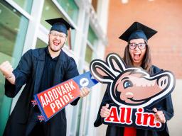 Aims students in cap and gown with All in and Aardvark Pride signs