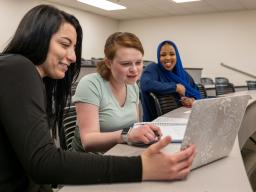 three students looking at a laptop in a classroom