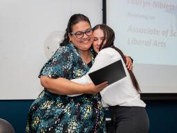Two women hugging as one receives a certificate