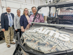 Four people posed with camouflaged utility task vehicle