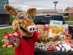 Arty Mascot posing with food donations in a truck