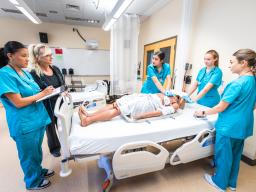 instructor and students standing around a hospital bed with mannequin patient