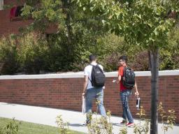 Two students walking on sidewalk next to brick wall