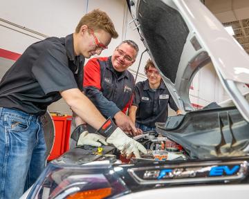 Aims students and an instructor work on an electric vehicle