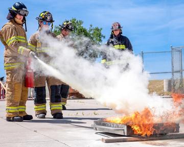 Three high school students use fire extinguishers to put out a securely contained fire. 