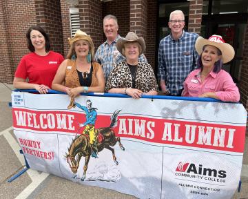 Group standing in front of sign saying, "Welcome Aims Alumni."