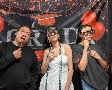 Three students posing in photo booth props at CDI Graduation