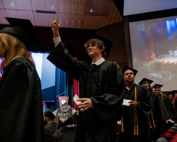 grads in caps and gowns walking to the stage male with hand in the air