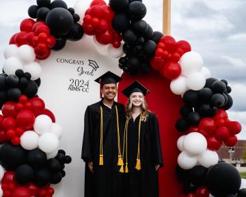 two grads posing with balloon display outside of welcome center