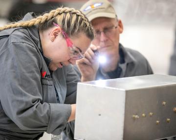 Aviation Maintenance Technician student works while supervised by instructor with flashlight