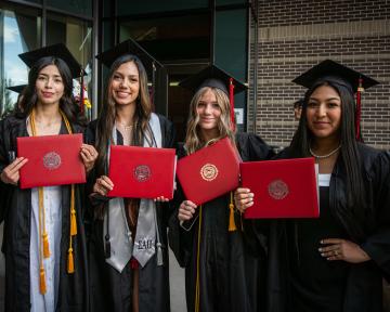4 graduates with diplomas after commencement 