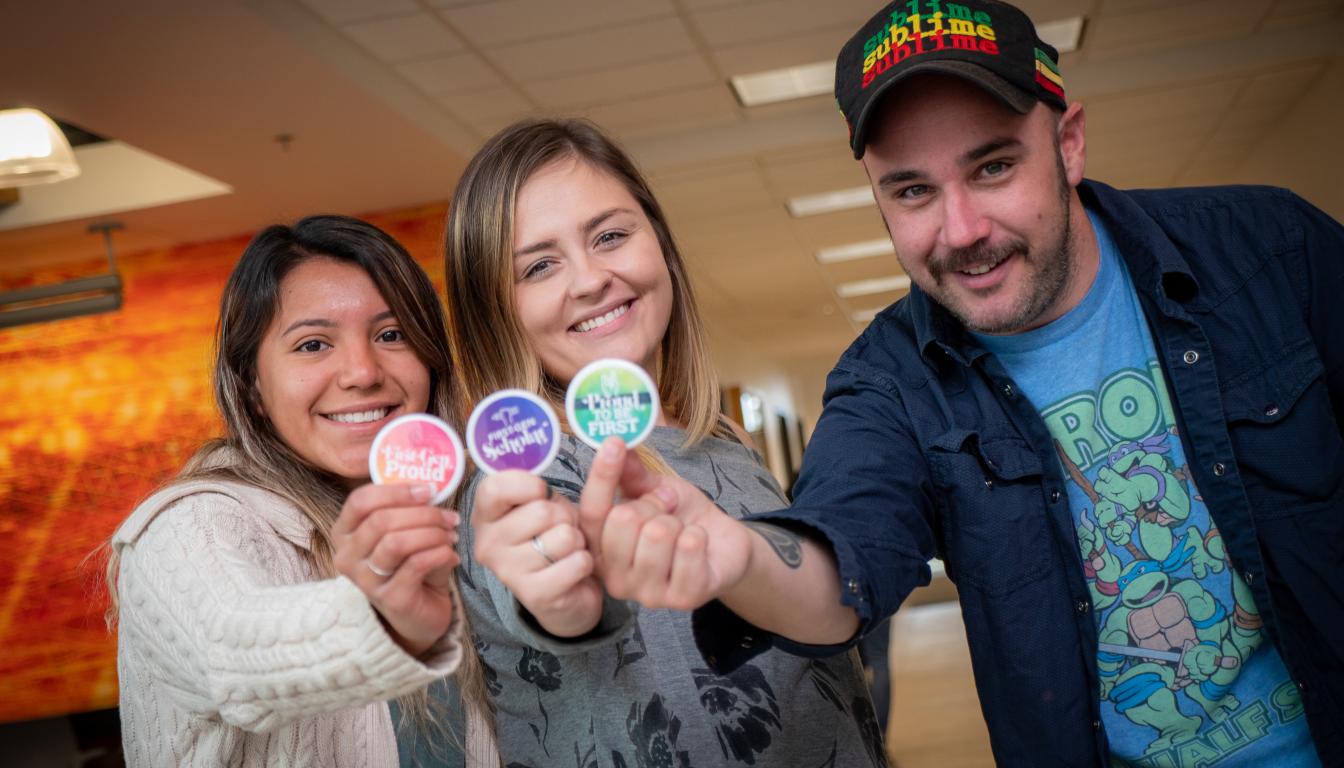 Students stand smiling at the camera, holding up First Generation pins