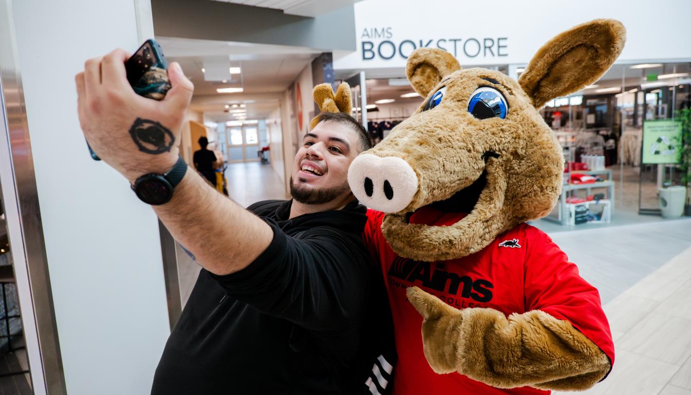 An Aims student takes a selfie with Arty, the Aims mascot