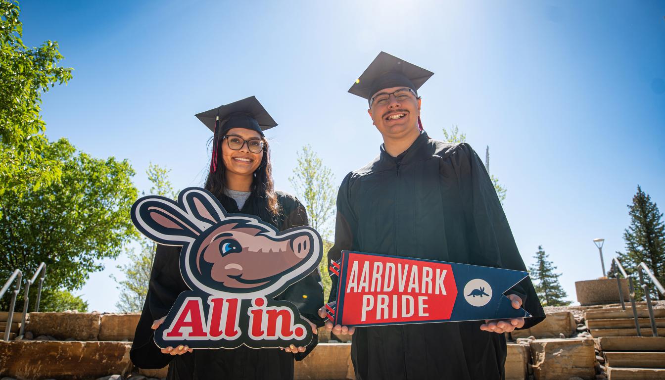 two students in cap and gowns with signs saying