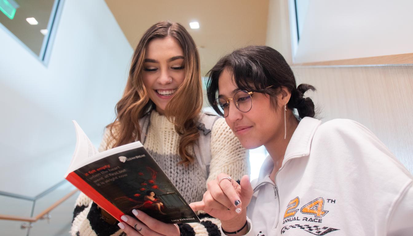 Two students look at a textbook together, and one of them points to something on the page.