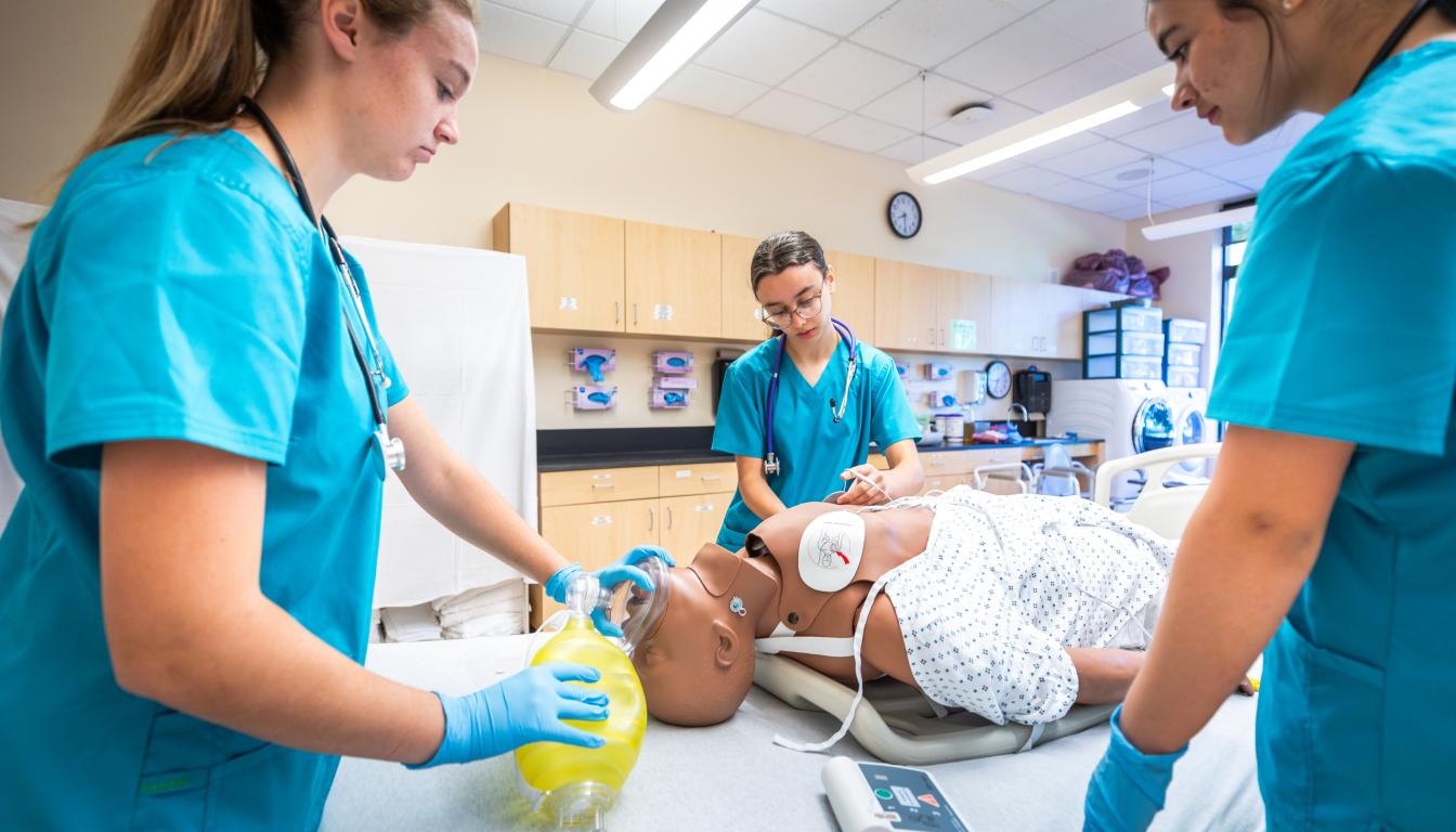 students practice emergency patient care on a medical manikin, using a bag-valve mask 