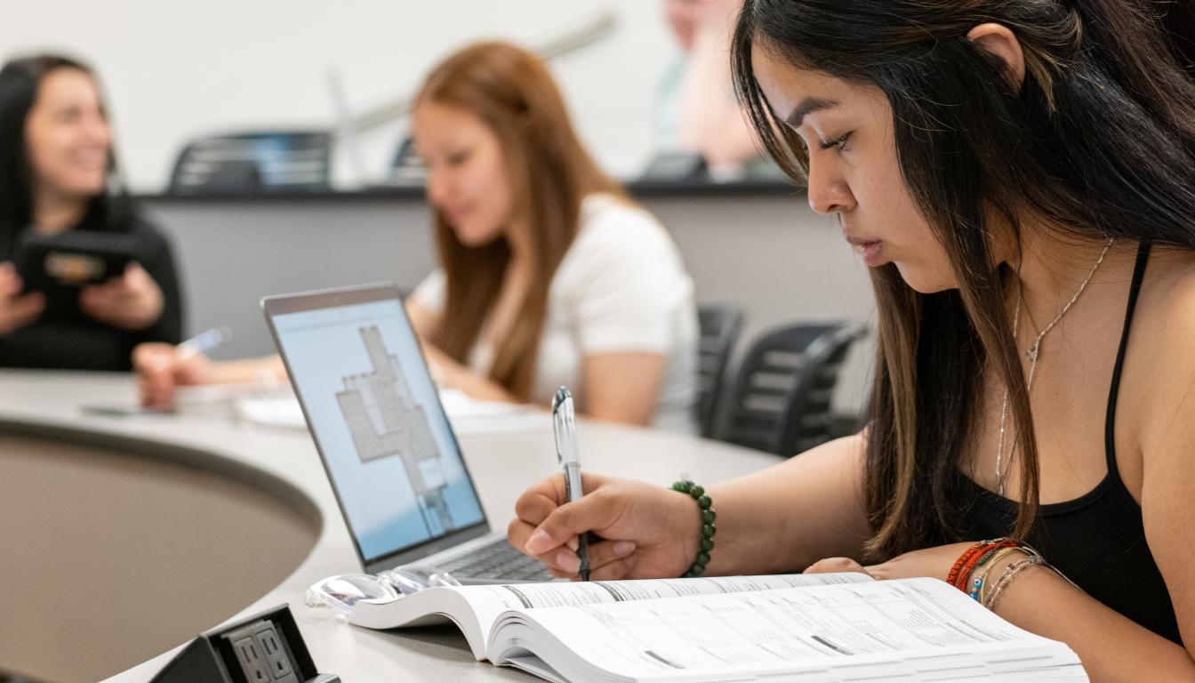 Four students sit at desks taking notes during a lecture for their college program at Aims.