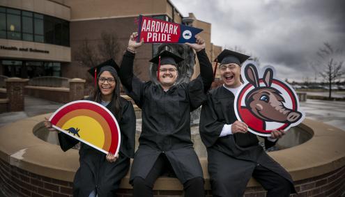 Aims students in cap and gowns with signs