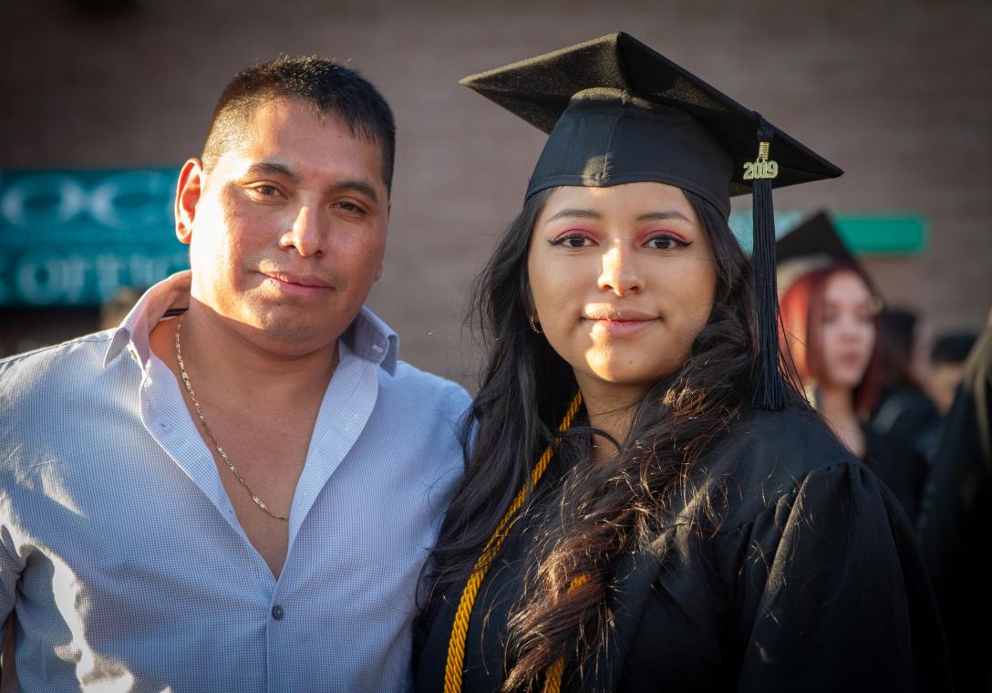 An Aims Community College graduate in cap and gown standing with a guest