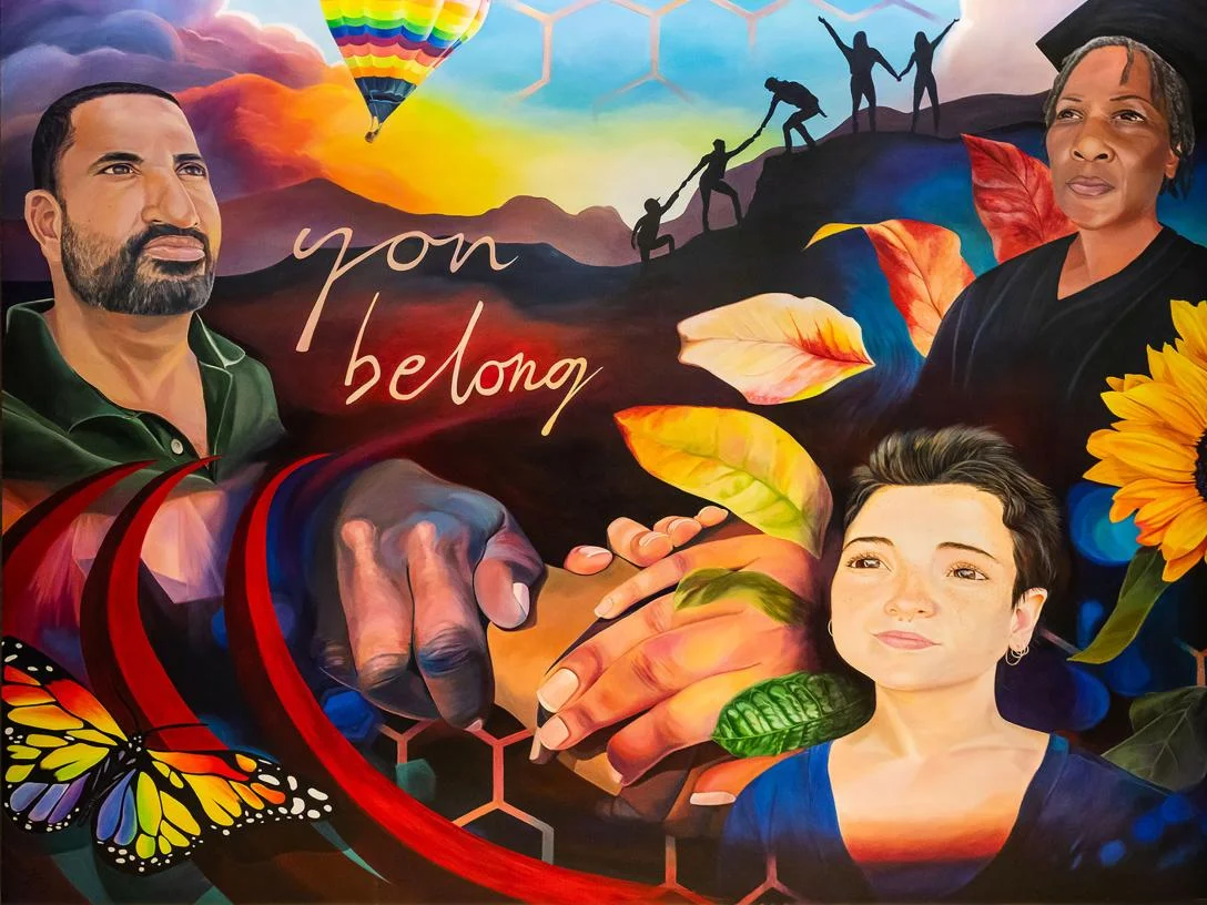 A colorful mural featuring people from many cultures and Aims landmarks on a wall in the Aims Community College Student Commons with the words “You Belong”