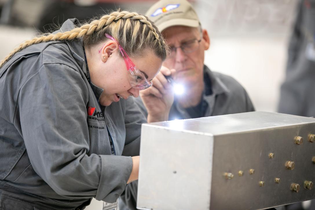 Aviation Maintenance Technician student works while supervised by instructor with flashlight