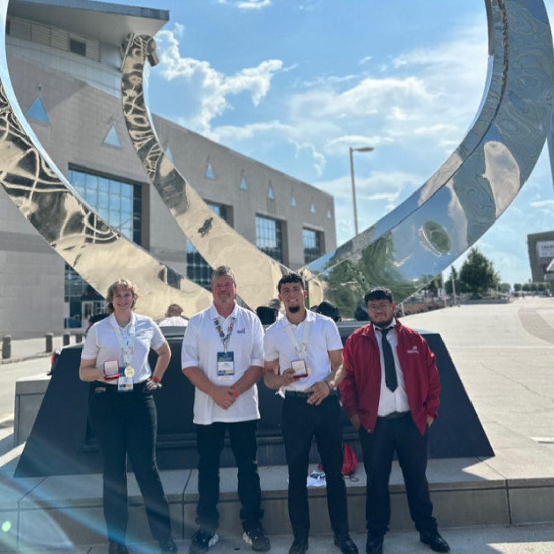 Four people standing with gold medals