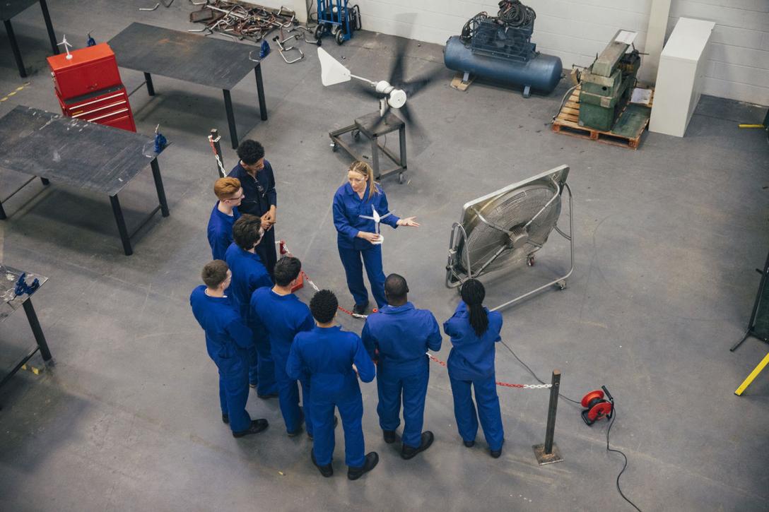 a group of aviation students in blue jumpsuits shot from above on the shop floor